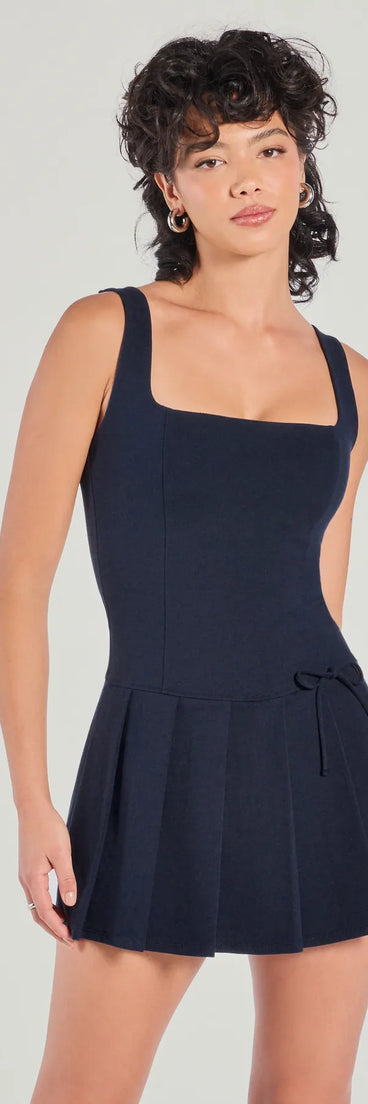 Flirty Girlie Bow Pleated Skirt Romper, a trendy navy blue mini dress featuring modern details and a fresh seasonal hue, perfect for creating chic 2025 looks.